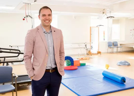 Man in pink jacket stands in rehabilitation gym