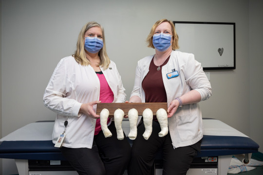 Nurses in masks stand holding a board with an array of small leg casts attached.