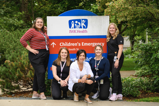 Five nurses stand and crouch around the IWK Health Children's Emergency sign.