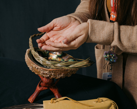 Cupped hands hover above a smudging bowl.