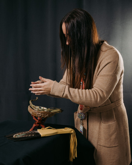 A woman brings her hands together above a smudging bowl.