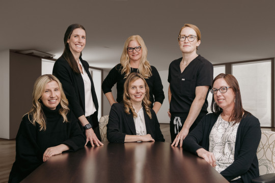 Six women sit and stand at a boardroom table.