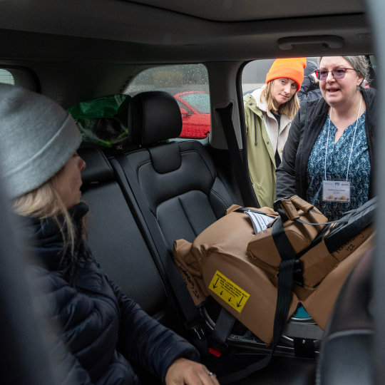 Child Safety Link instructors demonstrate the proper installation of a child car seat inside a vehicle to participants during an outdoor training session.