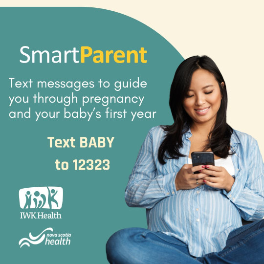 A pregnant woman sits cross-legged, smiling down at the phone in her hands.