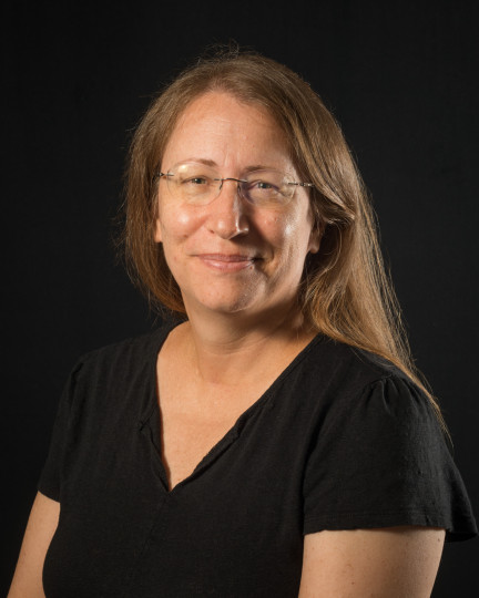 A light skinned woman in glasses and black top smiles at the camera.