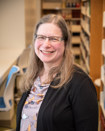 Smiling woman in glasses standing in a library.