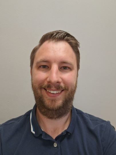 Man in dark blue polo shirt  smiles at camera.