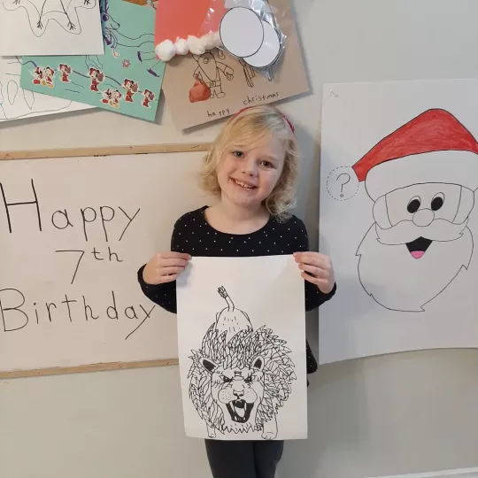 A smiling girl holds up a piece of her artwork featuring a growling lion.