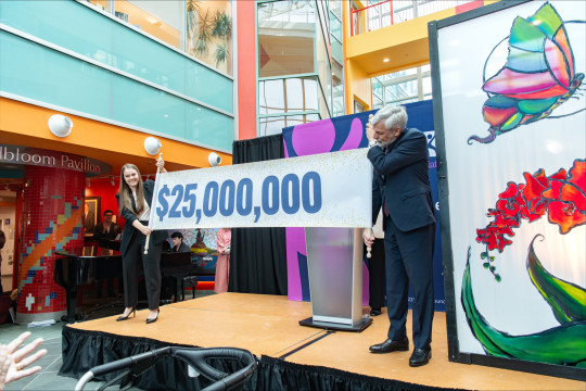 A man and woman stand on a stage and hold a banner with $25,000,000 printed across it.