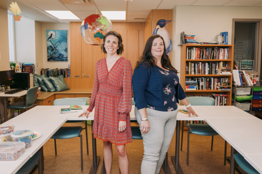 Two women stand in a bright cheery classroom.