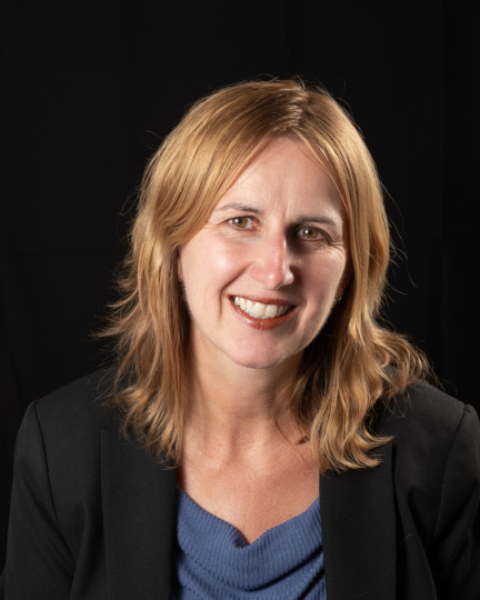 Smiling woman with blue top and black suit coat.