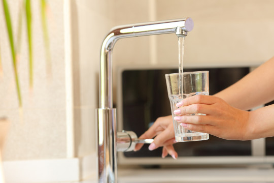 Hand holding a glass under flowing tap.