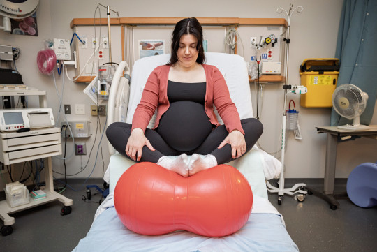 A pregnant Lauren sits on a hospital bed, feet up on a medicine ball.