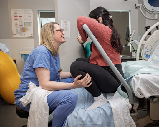Nurse Jennifer Jollymore sits on a hospital bed with pregnant Lauren, helping her with breathing.