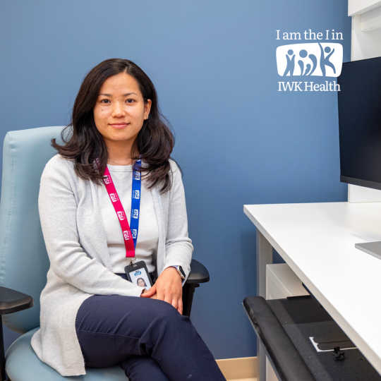 Sabina Thapa sits at a computer. I am the I in IWK logo is int he corner.