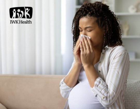 A pregnant African Canadian woman blows her nose.