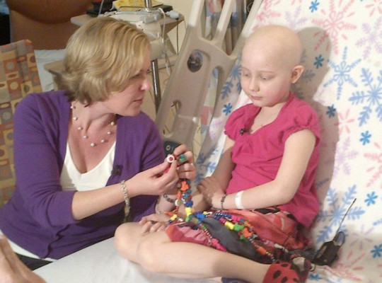 Tori sits on a hospital bed with an adult visitor.