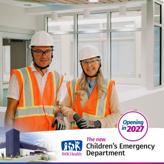 Brian and Katie stand in the under construction Emergency department wearing safety vests, helmets and goggles.