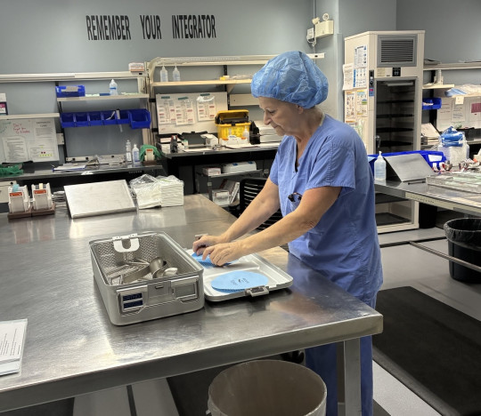 A technician in medical scrubs assembles a rigid sterilization box.