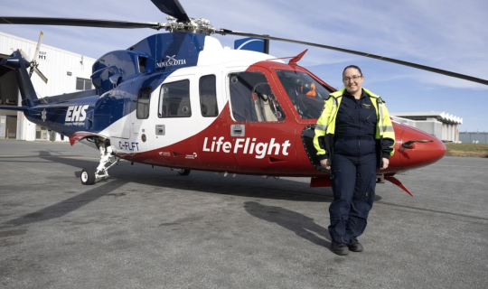 Respiratory therapist Jessica Carew stand beside a LifeFlight helicopter.