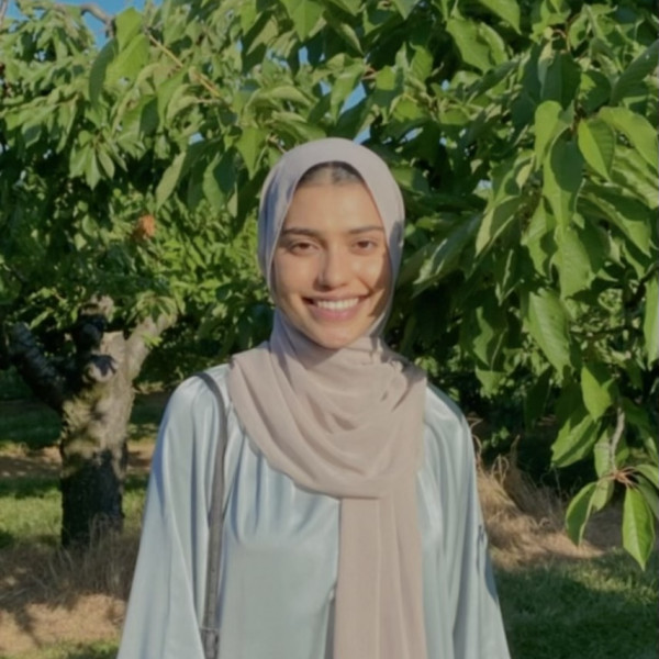 An image of Momina Raja smiling next to a tree.