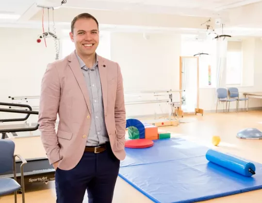 Man in pink jacket stands in rehabilitation gym
