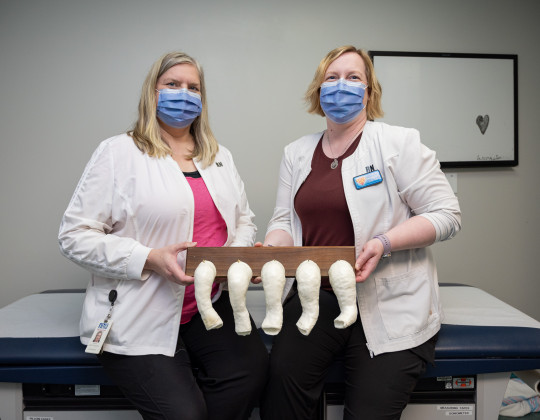 Nurses in masks stand holding a board with an array of small leg casts attached.
