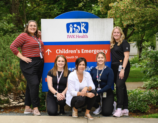 Five nurses stand and crouch around the IWK Health Children's Emergency sign.