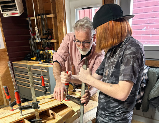 An older man and a youth apply clamps to a Stan up paddle board they are building.