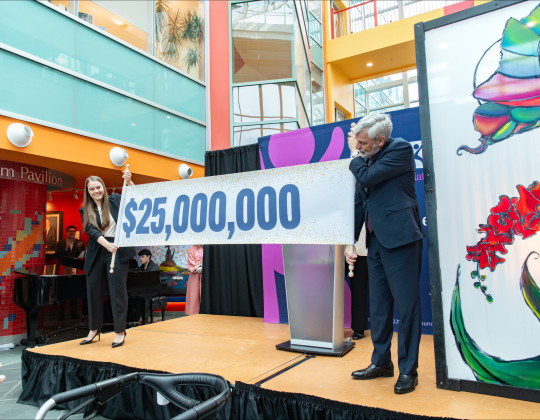 A man and woman stand on a stage and hold a banner with $25,000,000 printed across it.