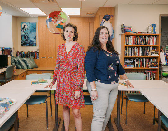 Two women stand in a bright cheery classroom.