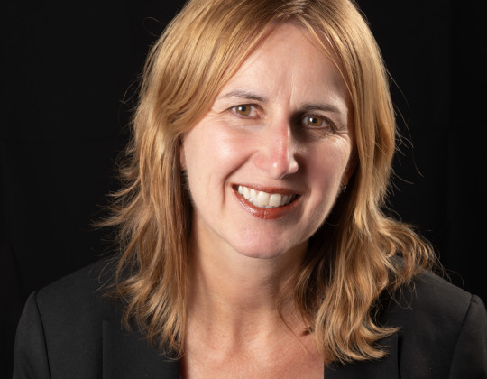 Smiling woman with blue top and black suit coat.