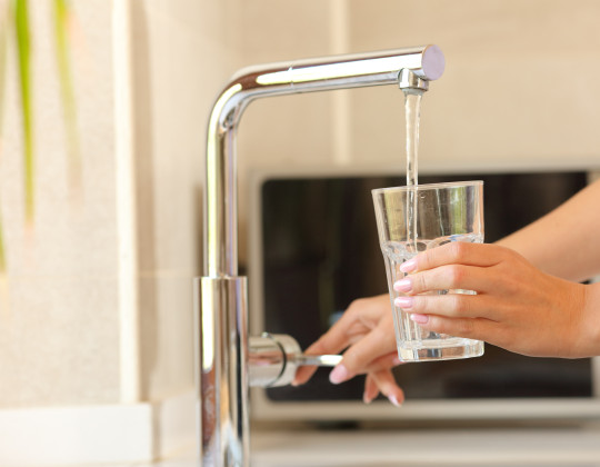 Hand holding a glass under flowing tap.