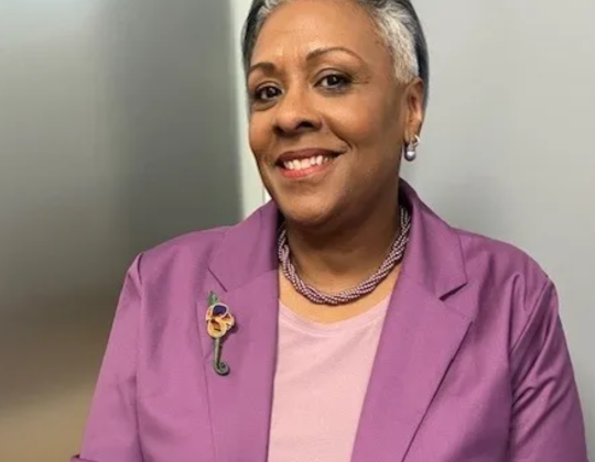 Angela Johnson in a purple suit, smiling at the camera. 