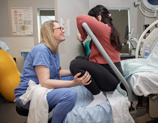Nurse Jennifer Jollymore sits on a hospital bed with pregnant Lauren, helping her with breathing.