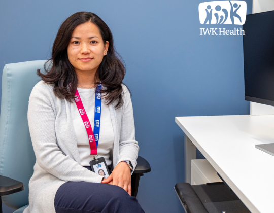 Sabina Thapa sits at a computer. I am the I in IWK logo is int he corner.