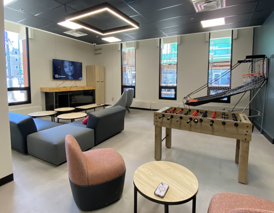 A youth friendly space with comfy modular chairs and couches, a foosball table and basketball game.