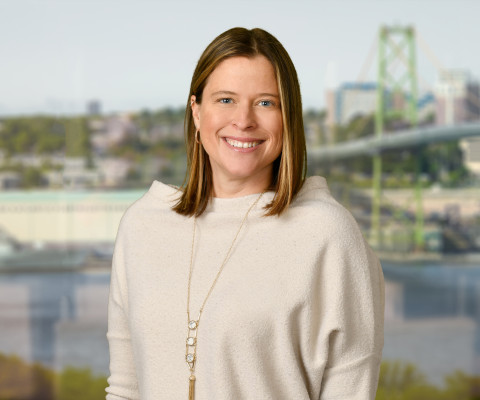Lindsay Hawker smiling in front of the harbour and bridge wearing a cream sweater