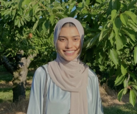 An image of Momina Raja smiling next to a tree.